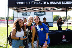 Three students stand in front of a School of Health & Human Sciences tent on the IUPUI campus.